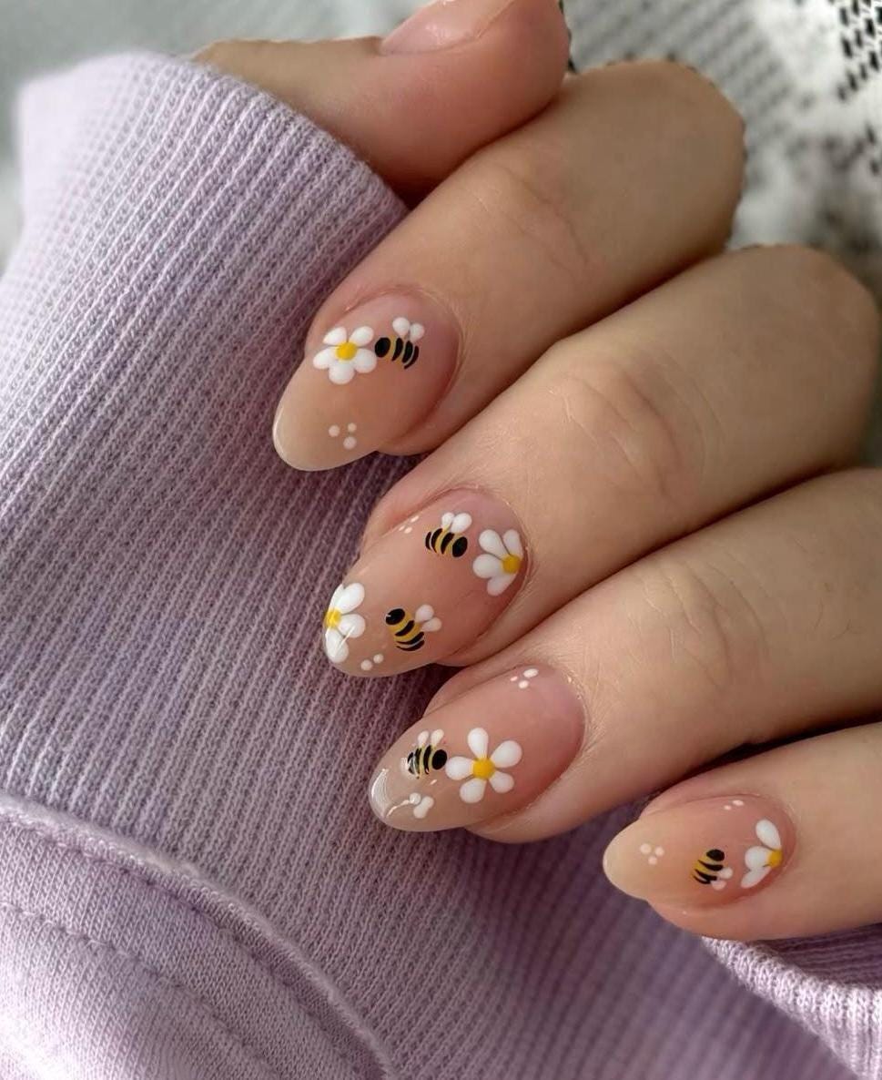 May include: Almond shaped nails with a light pink base and white daisy and bee designs.