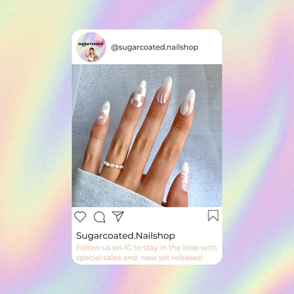 a close-up of a person&#39;s hand with long, white nail polish. The nails are painted with a white and silver design, and the person is wearing a ring. The background is a gradient of pink and purple colors.